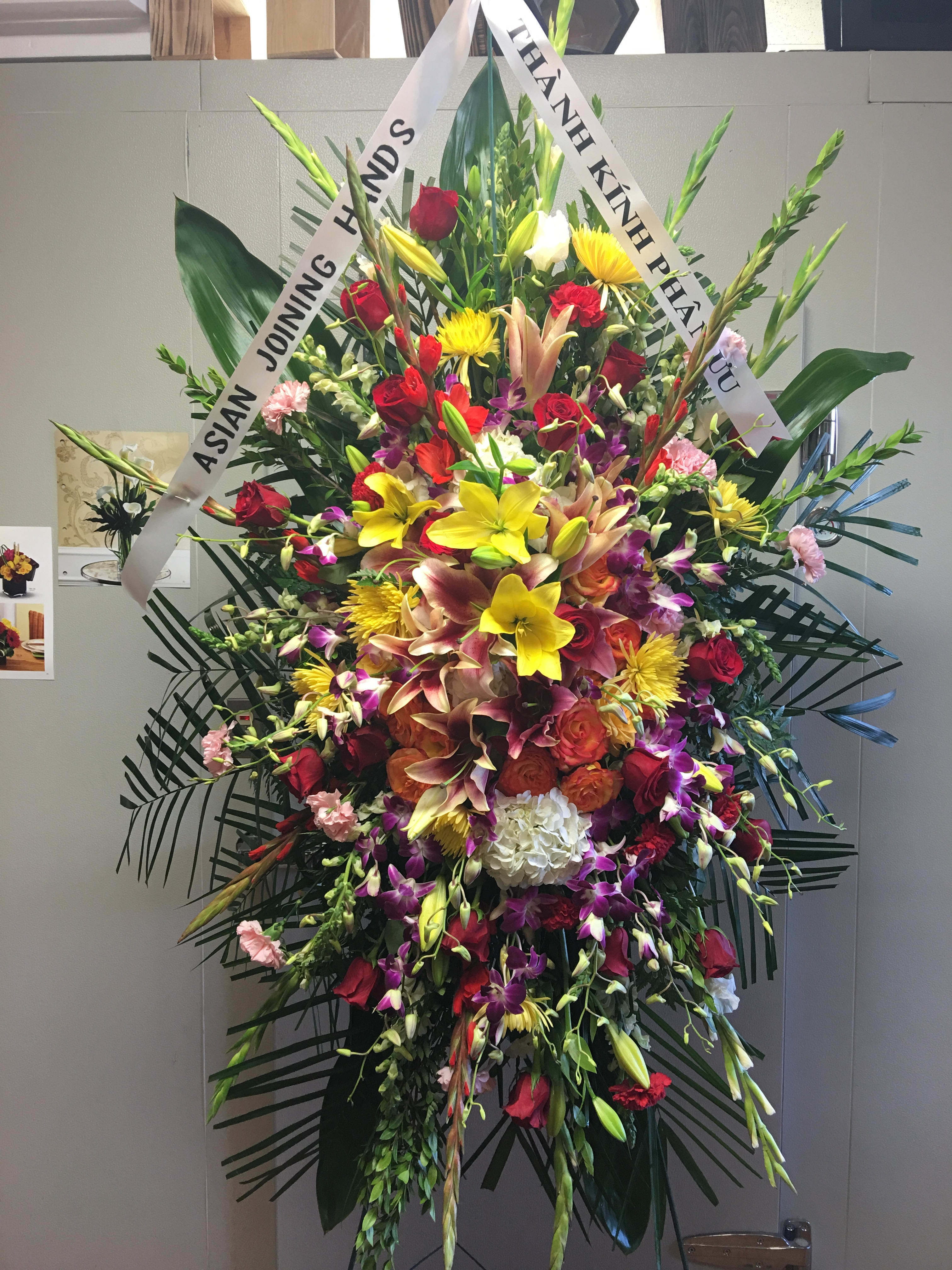 Large standing floral spray with mixed blooms and white condolence ribbons