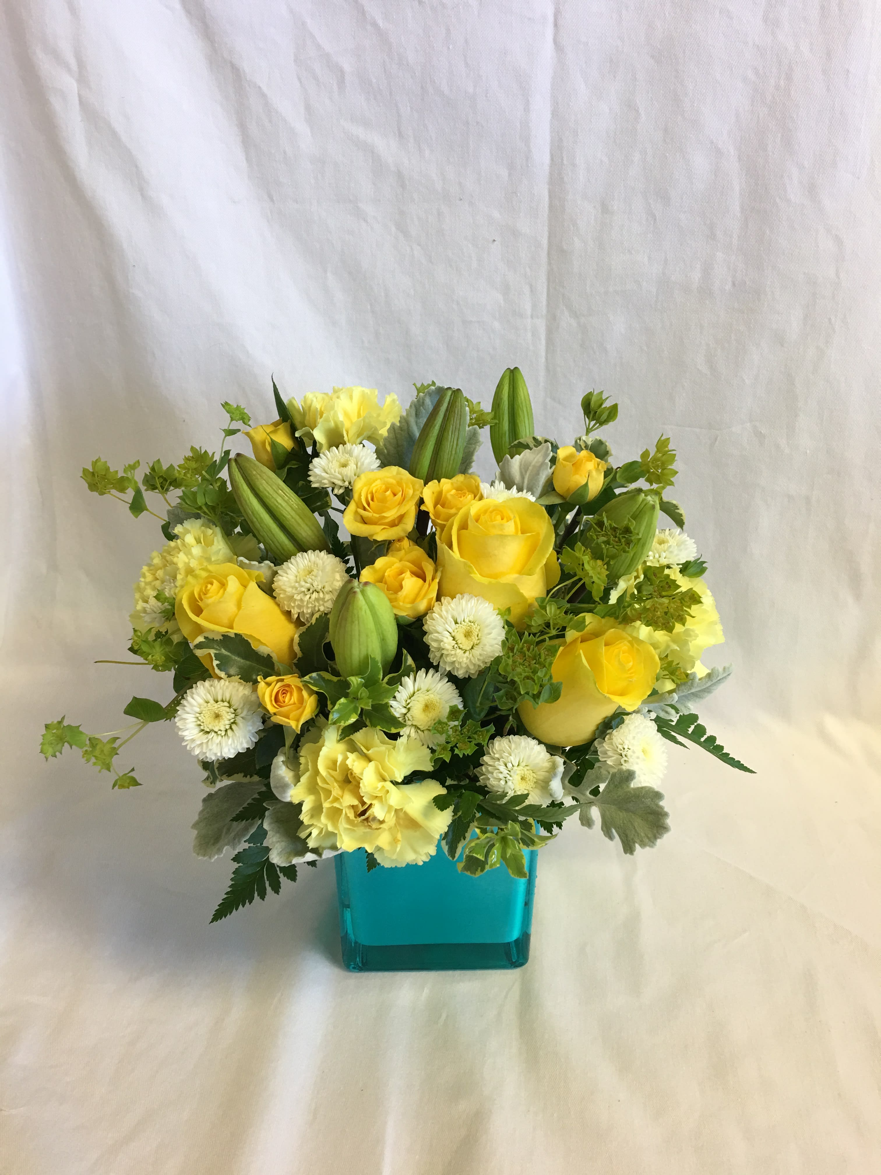 Yellow roses and white pom flowers in a turquoise vase