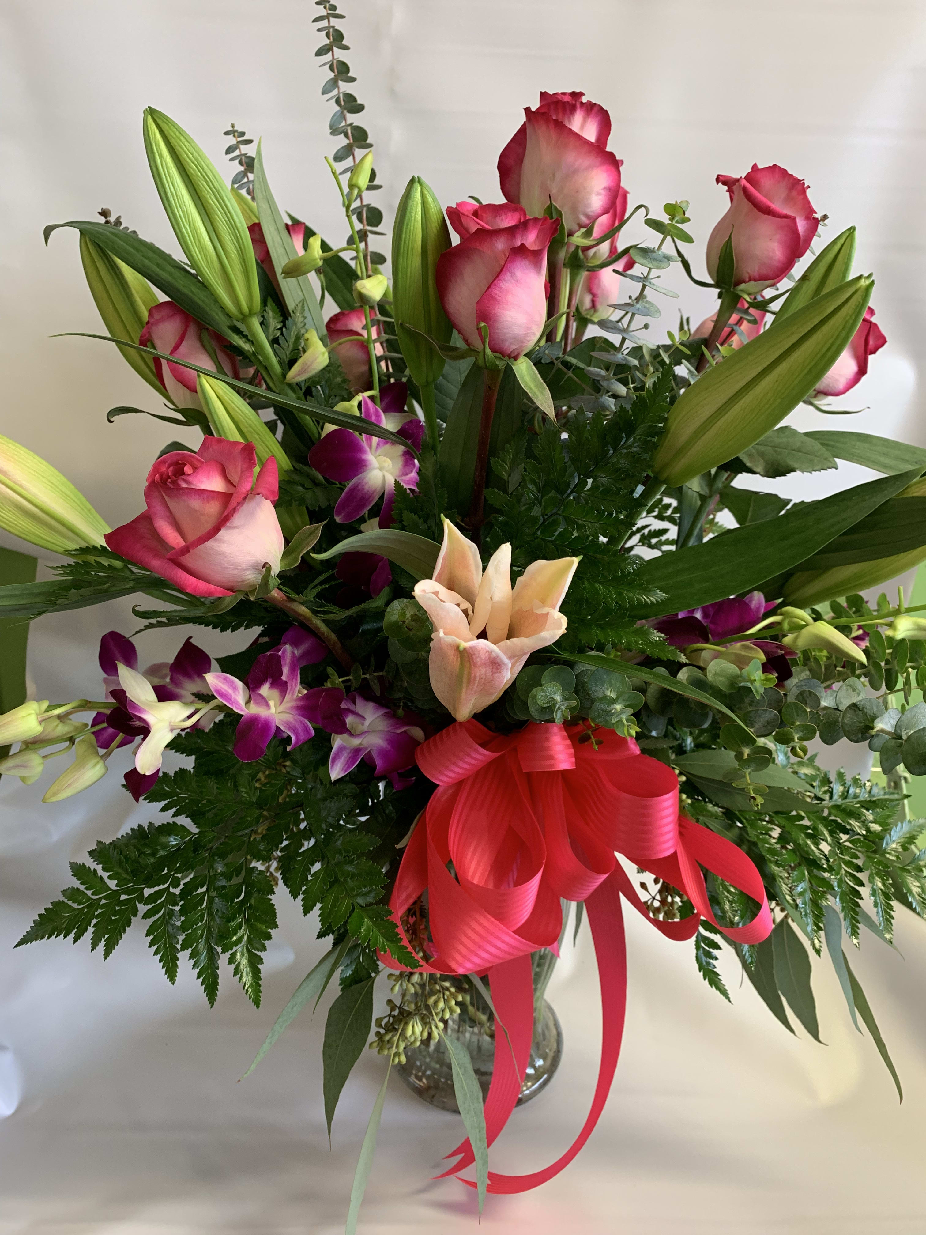 Bouquet of pink roses, lilies, and purple orchids in a glass vase