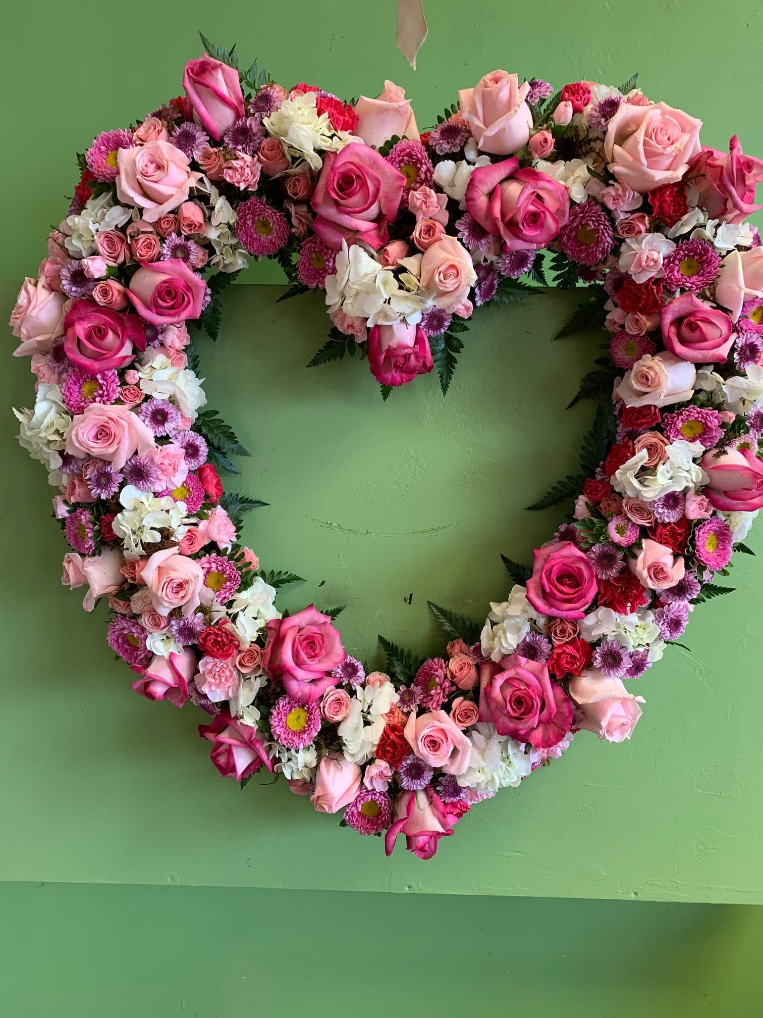 Heart-shaped floral wreath of pink and white roses on a green wall