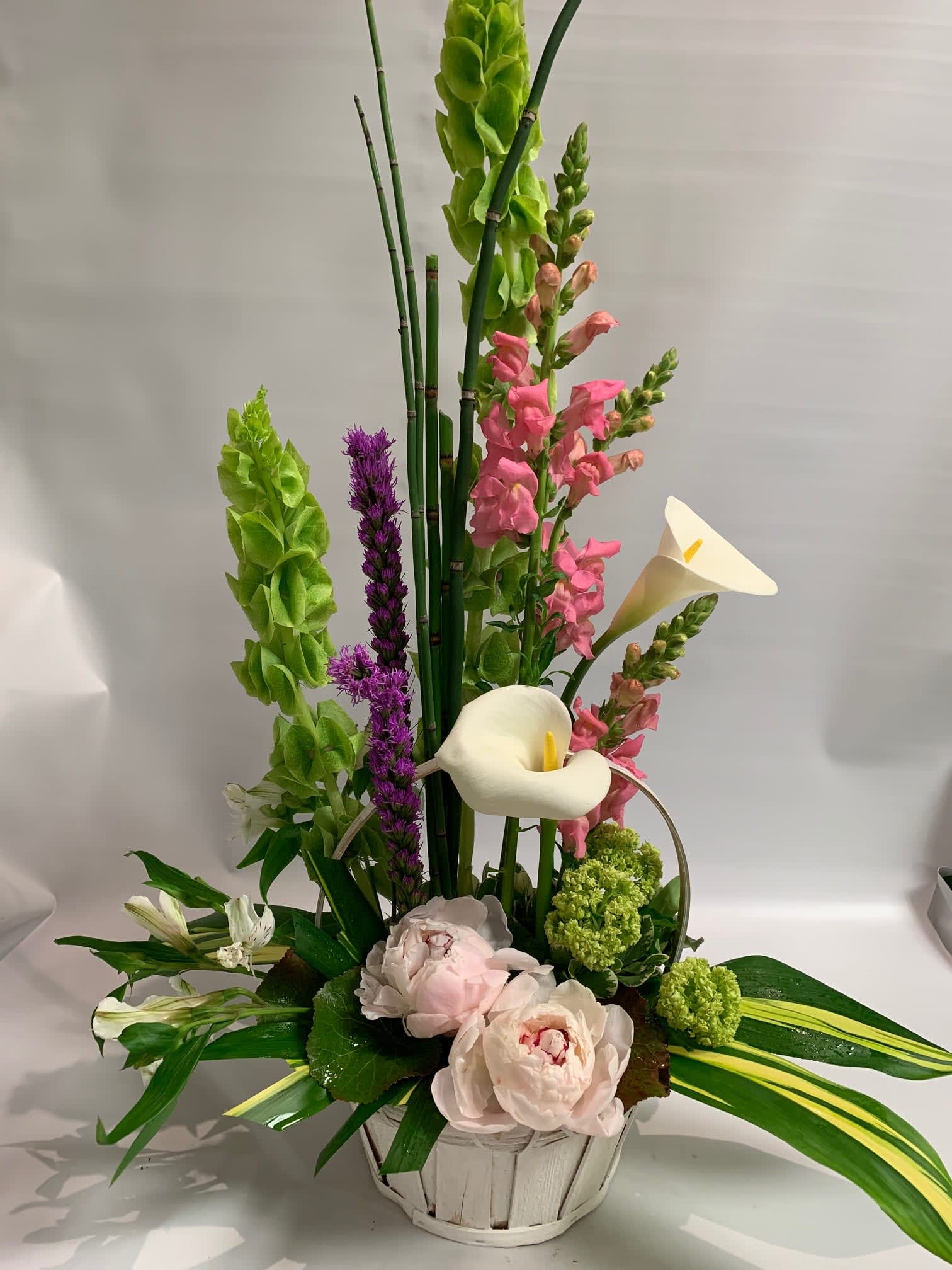 Tall floral arrangement with white calla lilies, pink blooms, and green spikes in a white basket