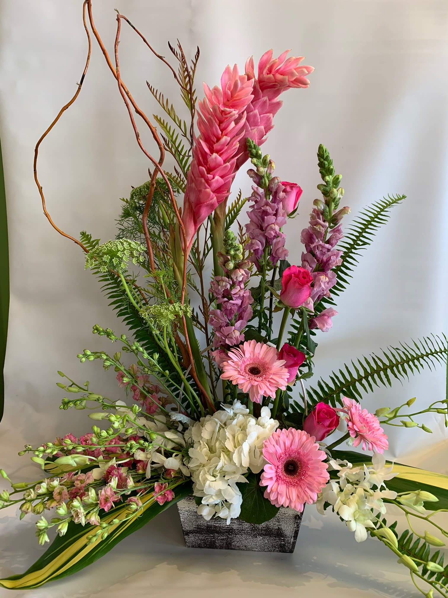 Tall pink floral arrangement in a rectangular vase with gerberas and orchids
