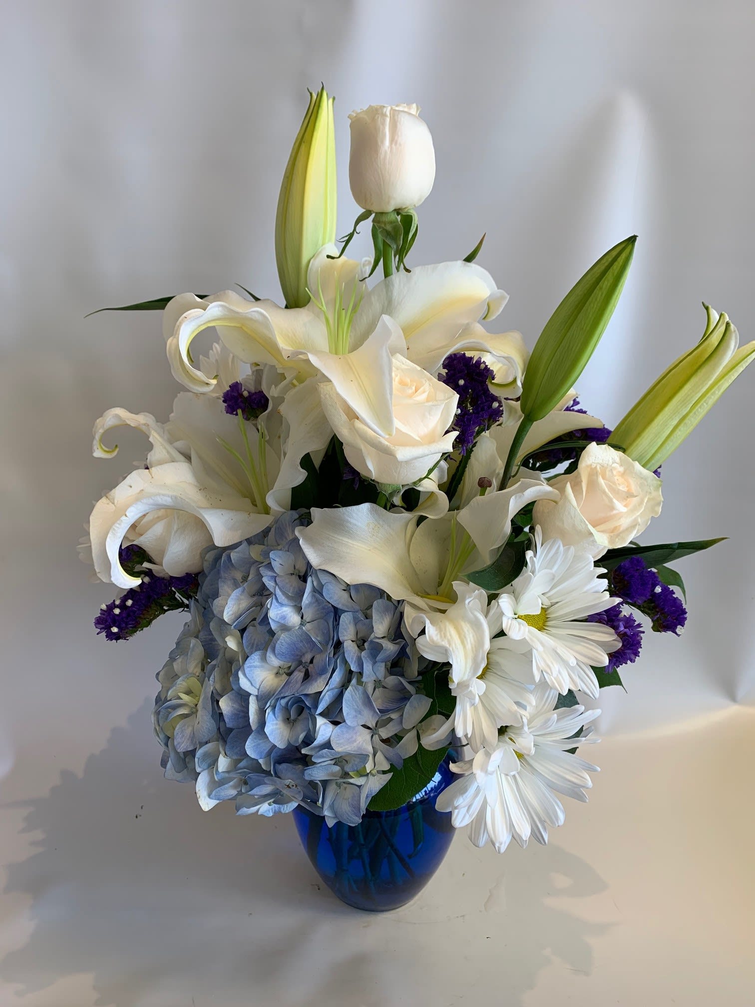 White lilies, roses, and blue hydrangea in a blue vase