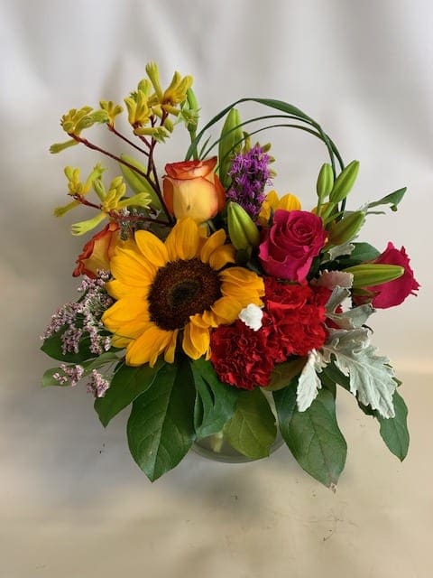 Mixed bouquet with a sunflower, roses, lilies, and carnations in a glass vase