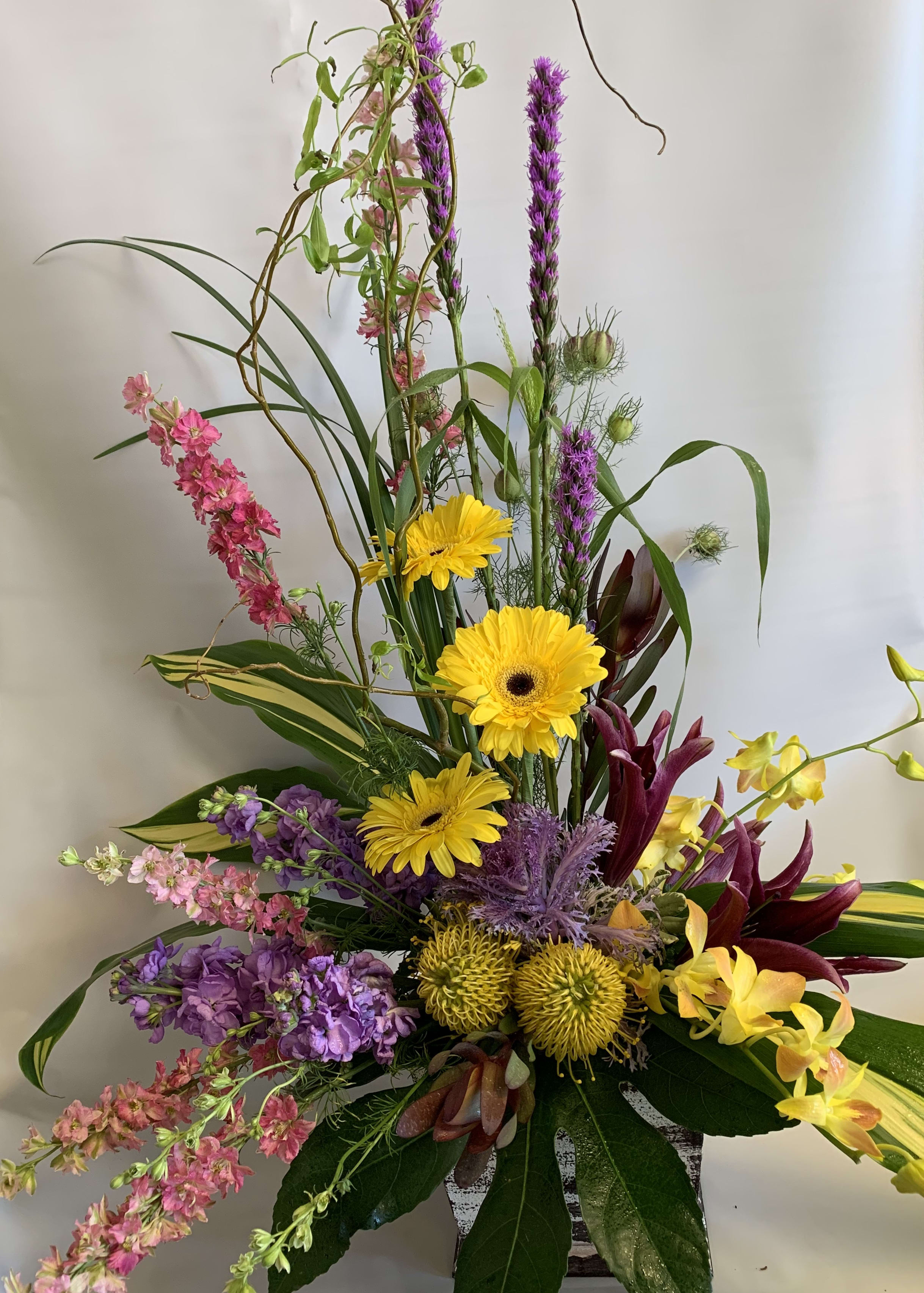 Tall mixed bouquet with yellow gerberas, purple blooms, and pink flowers