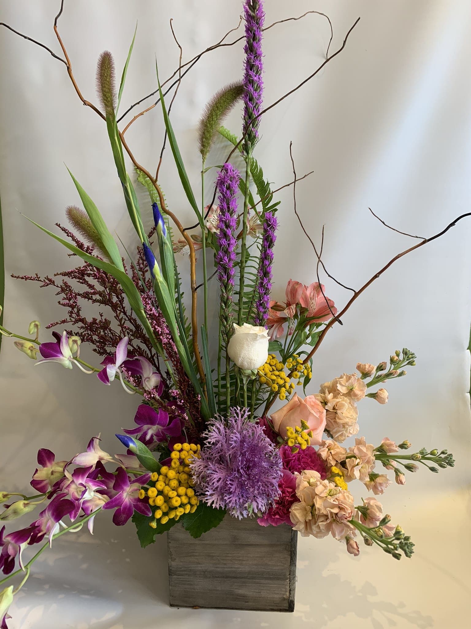 Tall mixed floral arrangement in a wooden box with purple orchids and peach blooms