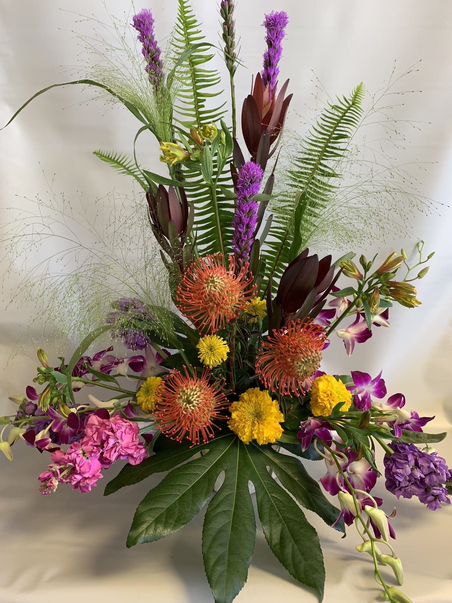 Tall tropical bouquet with purple orchids and orange pincushion blooms