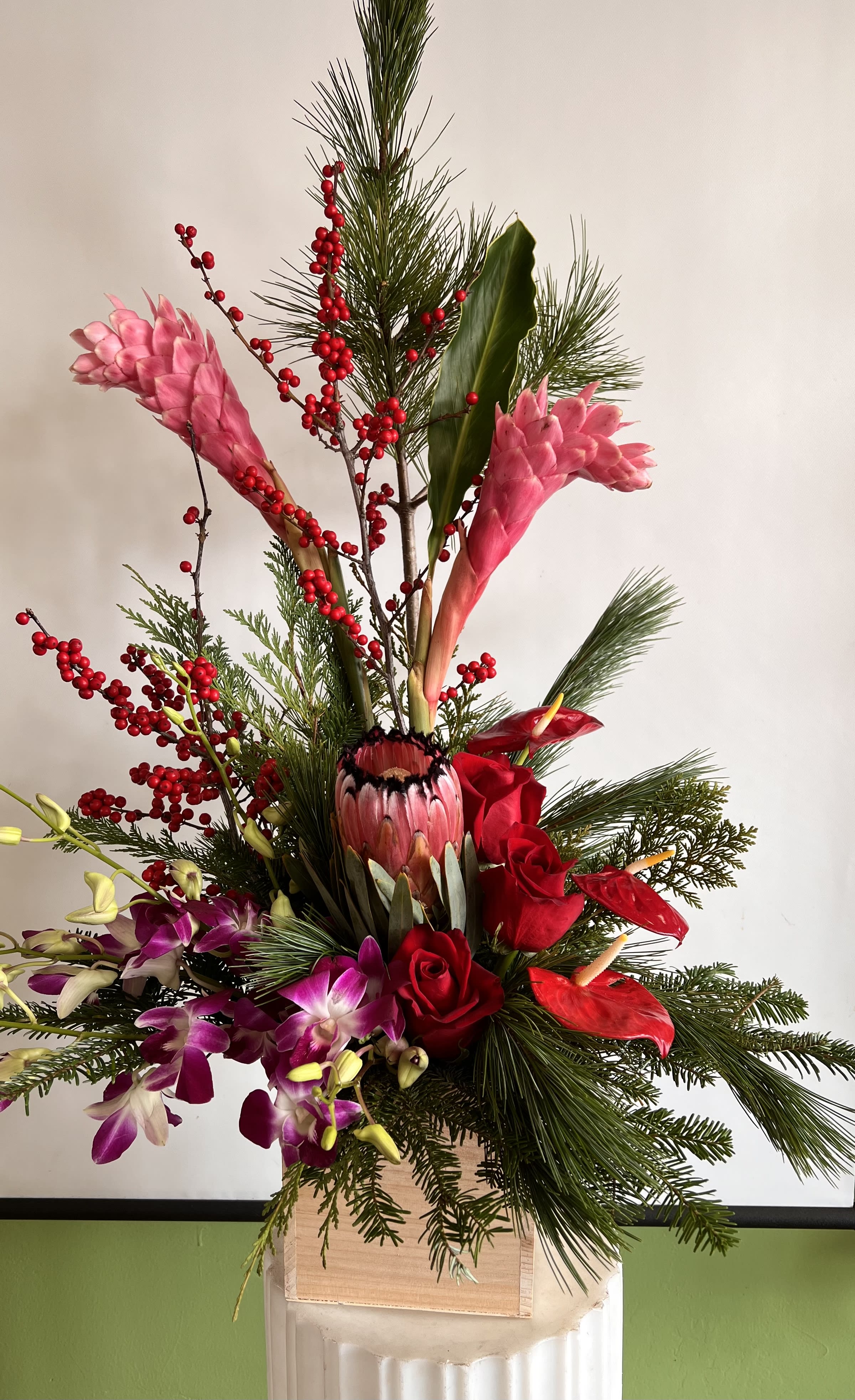 Tall tropical arrangement with pink ginger, red roses, and orchids in a wooden container