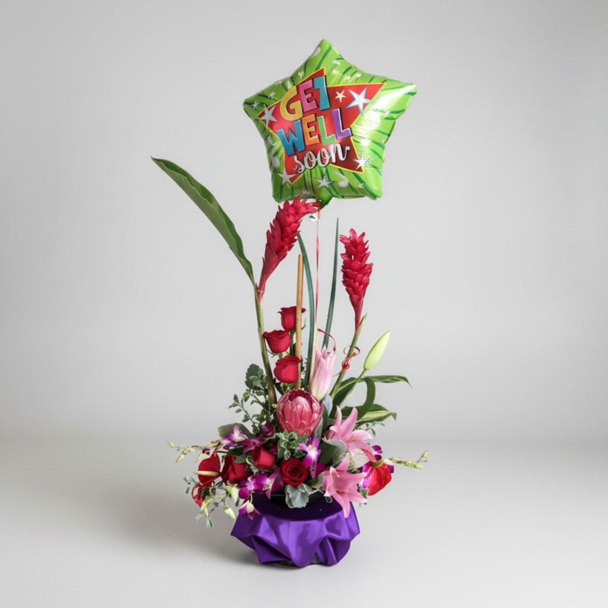 Tall floral arrangement with a green "Get Well Soon" balloon and purple base wrap