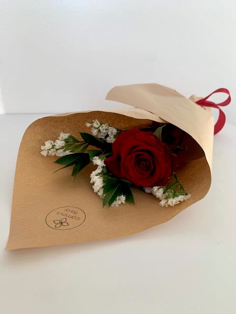 Single red rose wrapped in brown paper with white filler flowers