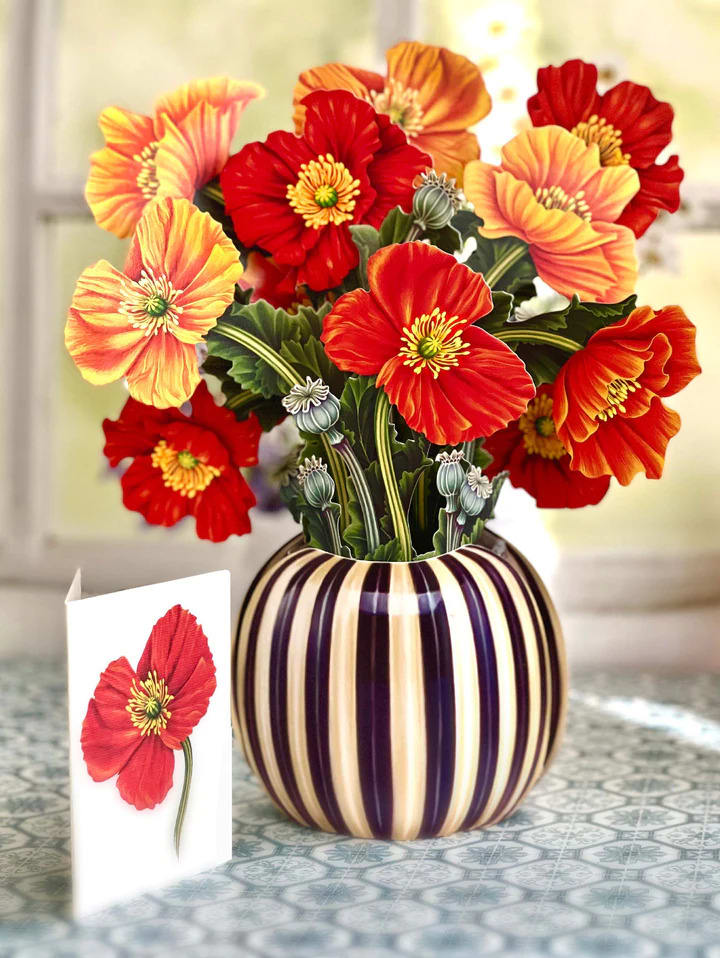 Bouquet of red and orange poppy-like flowers in a striped vase with a card