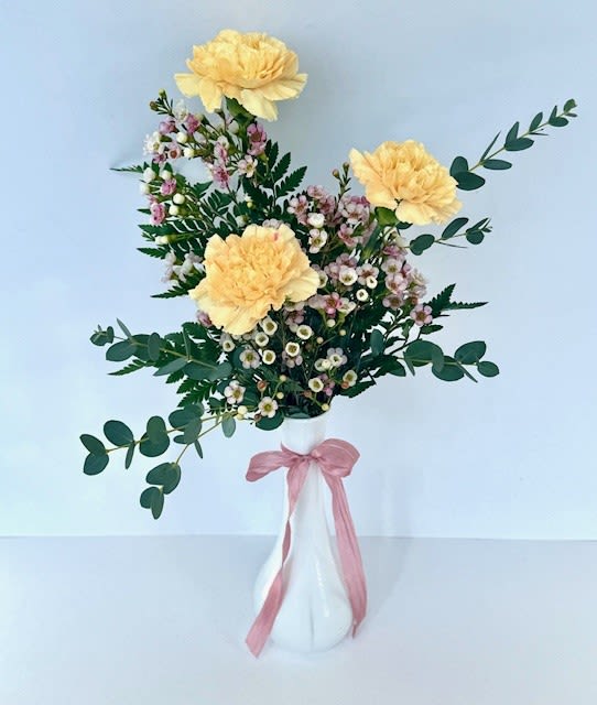 Yellow flowers in a white vase with a pink ribbon