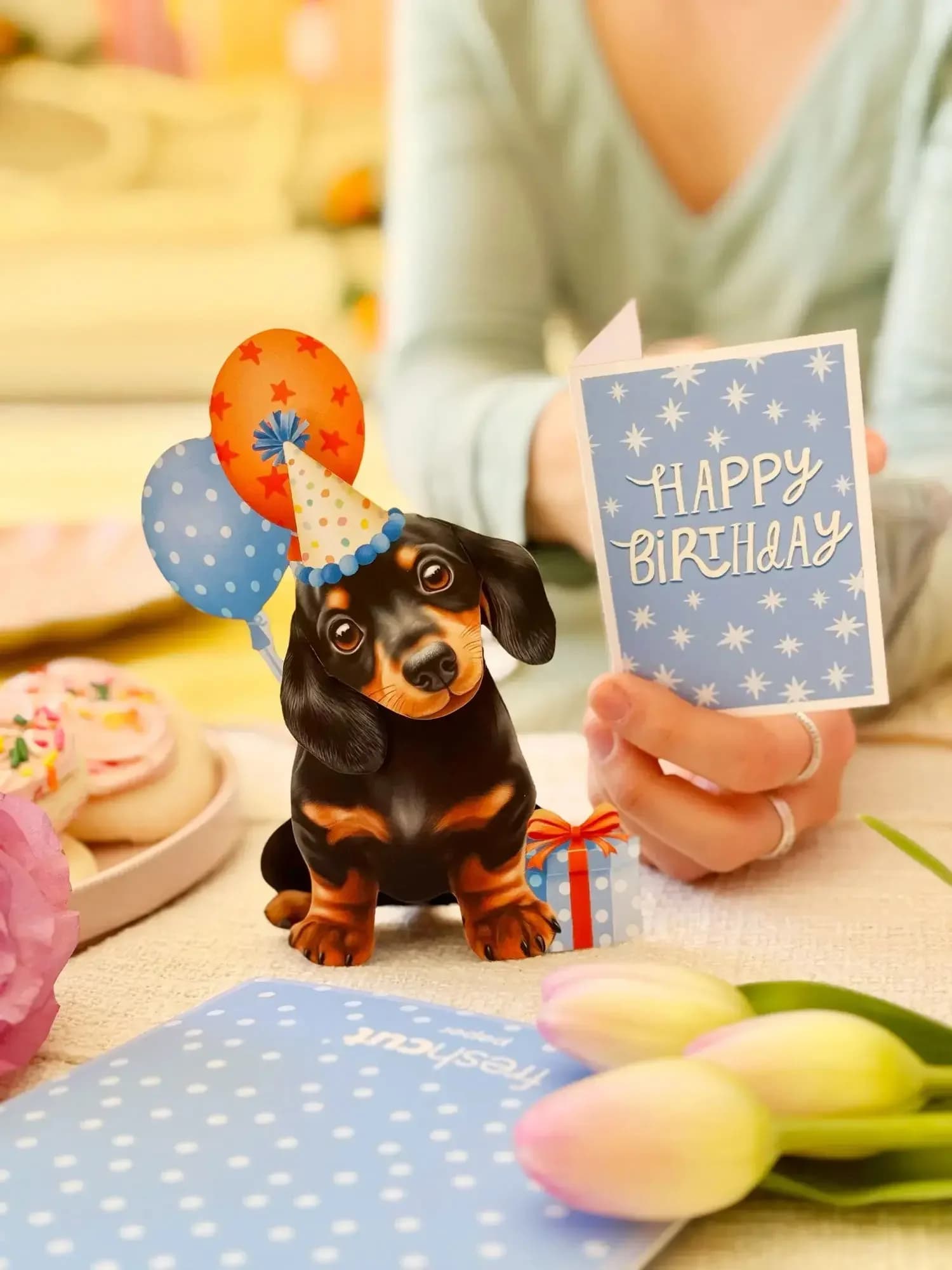 Mini Birthday Puppy Pop-Up Card - Meet our Mini Pop-Up Birthday Puppy — a playful pop-up birthday card that’s ready to party! All dressed up with bright balloons, a polka dot party hat, and a wrapped gift, this adorable little dachshund makes the perfect surprise for dog lovers. This cheerful mini pop-up greeting card is sure to bring smiles and is a festive way to wish loved ones well on their birthday.  Measures approx 5.5” high by 4.5" across