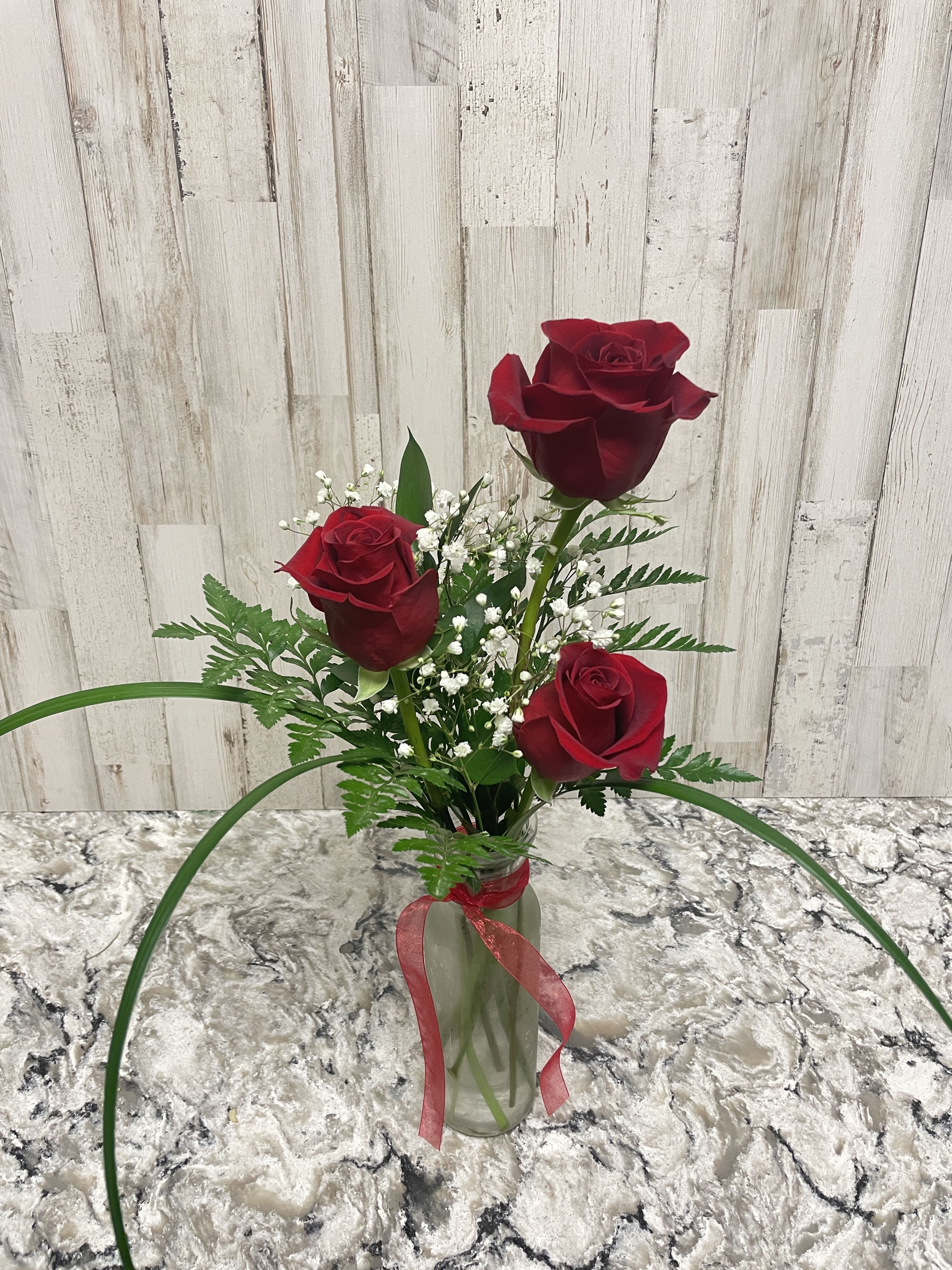 Three red roses in a glass vase with baby's breath and a red ribbon