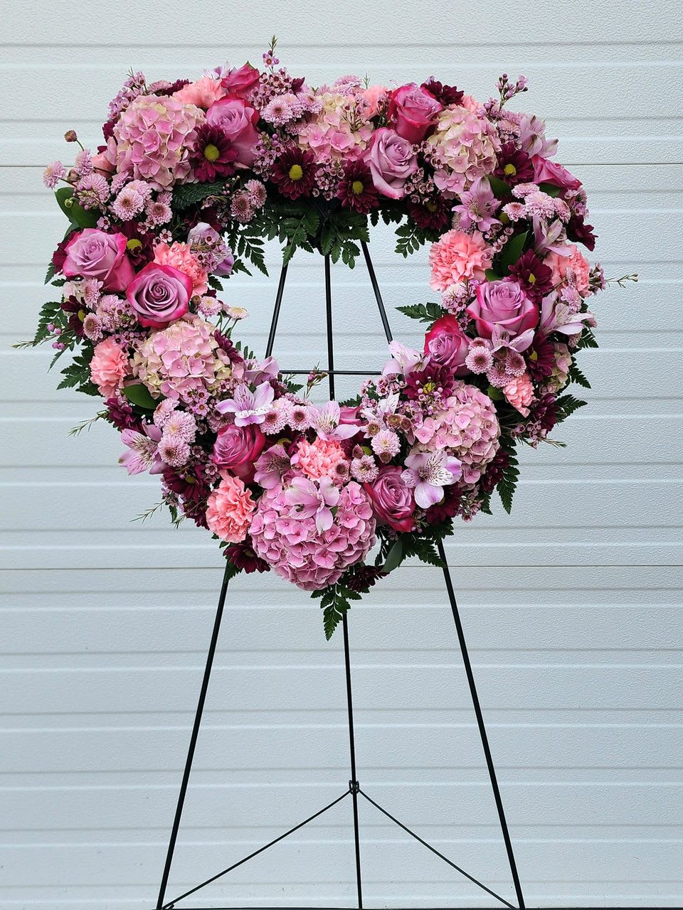 Heart-shaped floral wreath on a black stand with pink and purple blooms