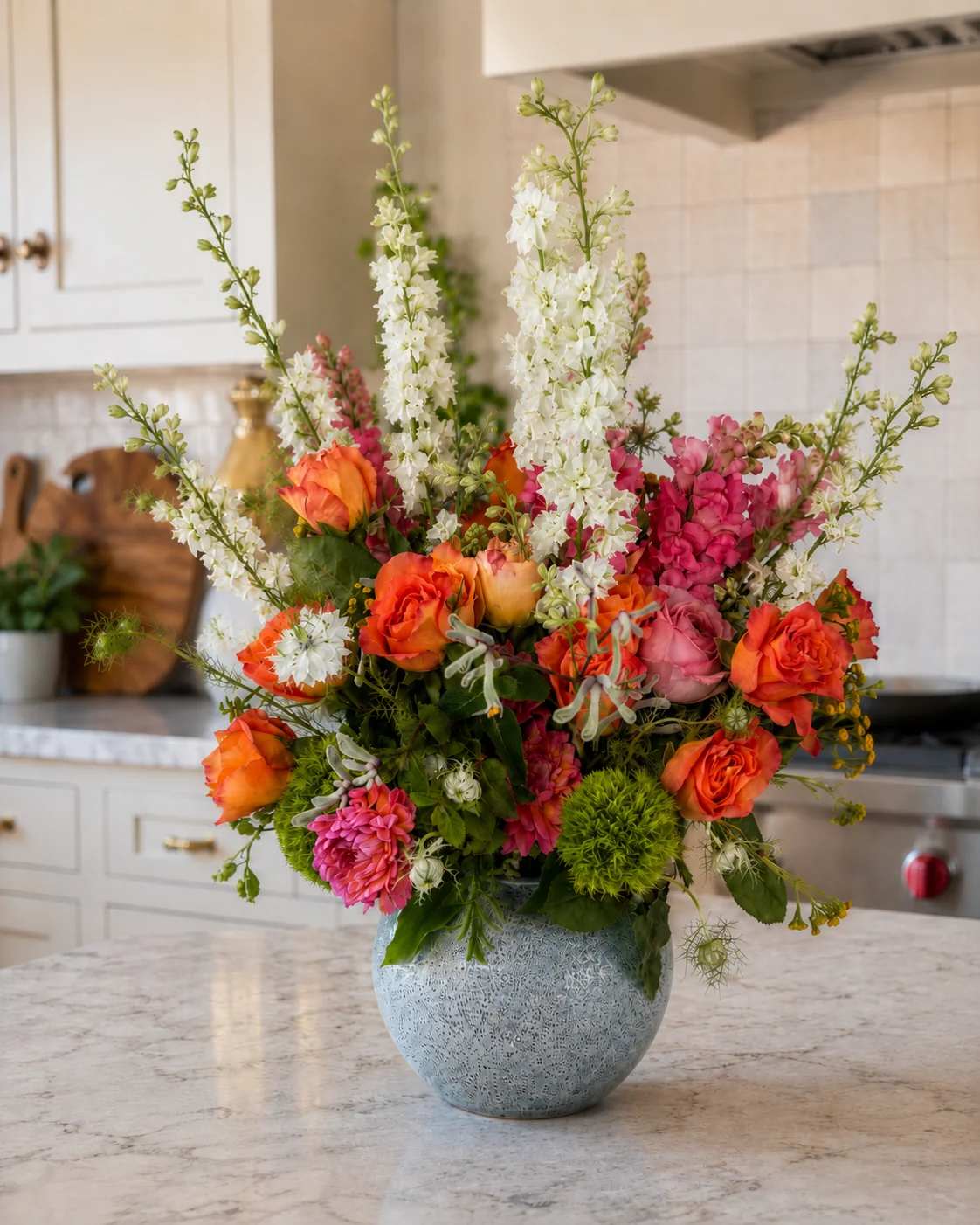 Colorful bouquet of orange roses, pink blooms, and white spikes in a blue vase