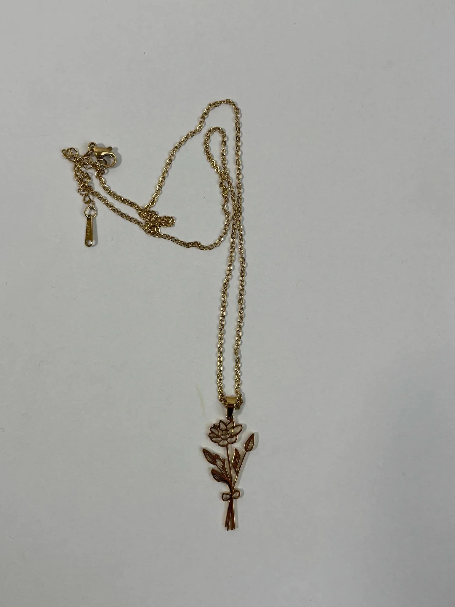 Gold-tone necklace with a floral pendant on a plain background