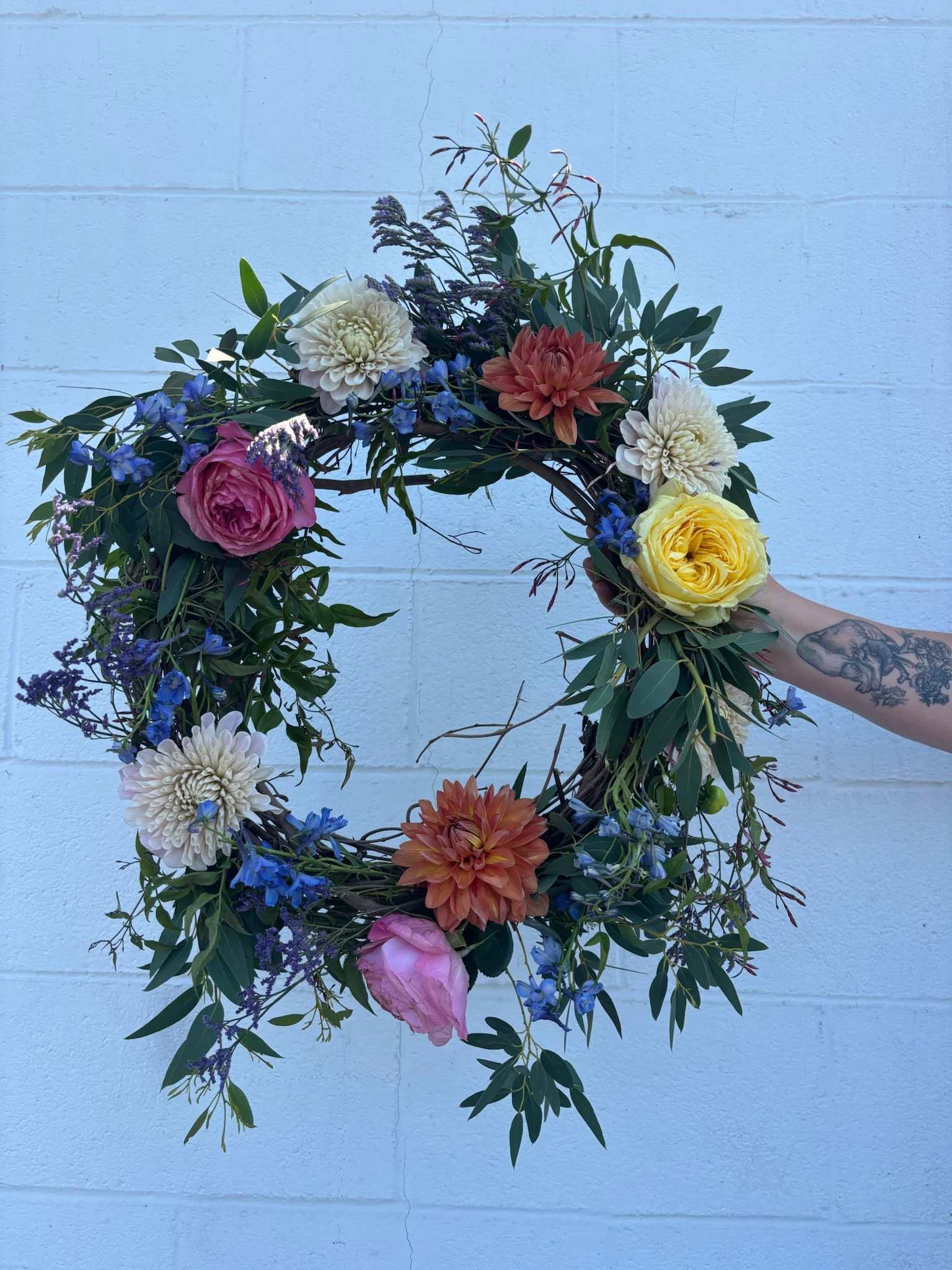Circular floral wreath with roses, dahlias, and blue flowers