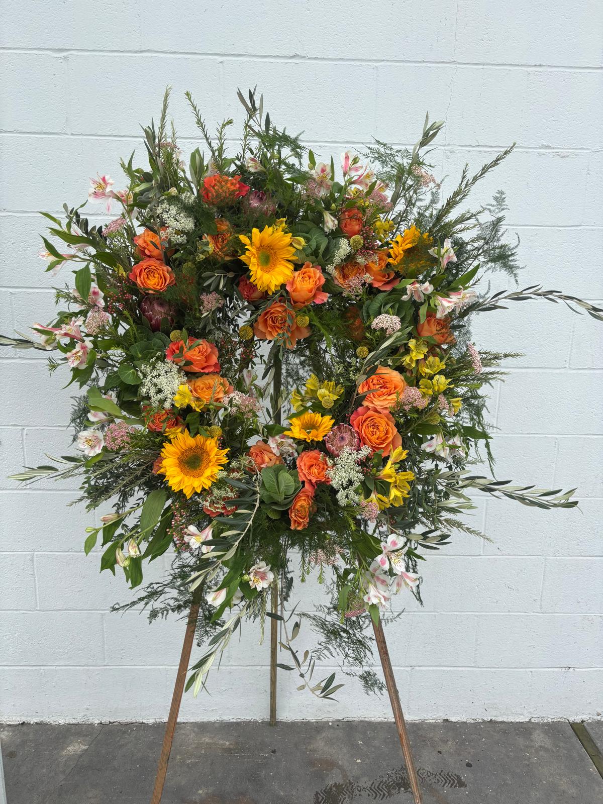 Large floral wreath on a stand with orange roses and yellow sunflowers