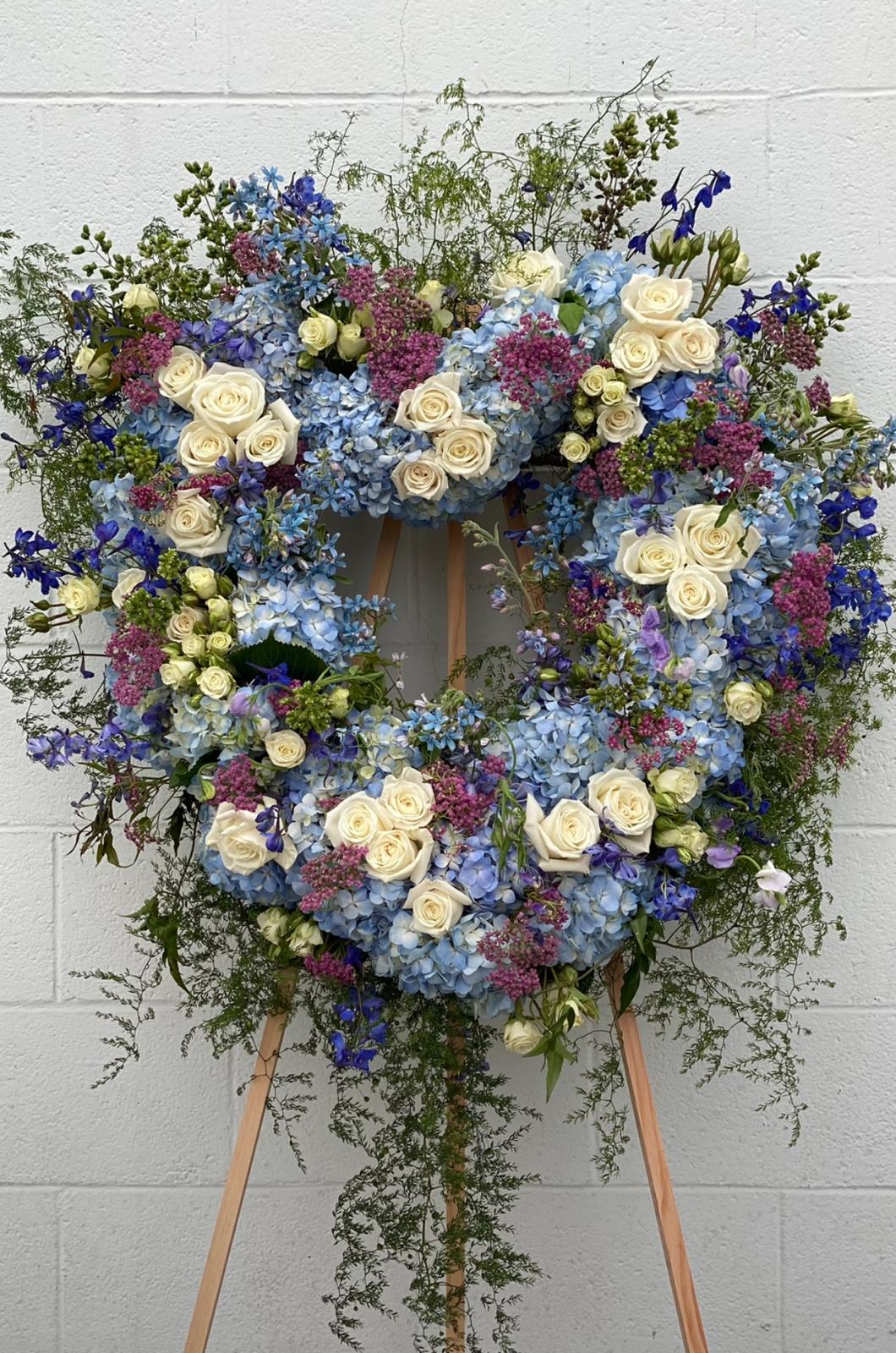 Large floral wreath of blue hydrangeas, white roses, and purple flowers on an easel