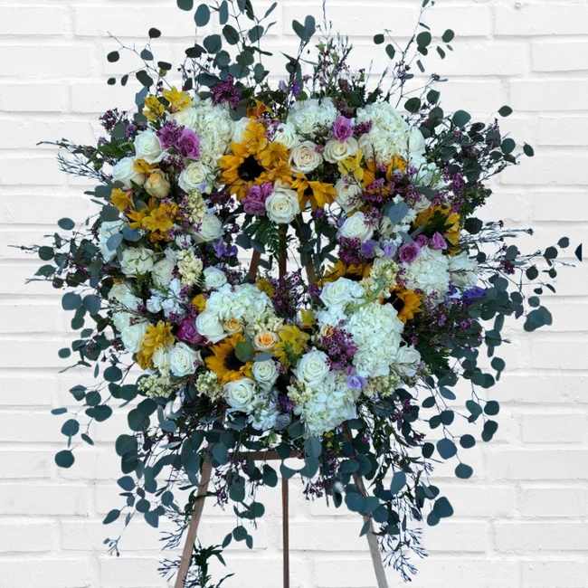 Large floral wreath on an easel with white, yellow, and purple flowers