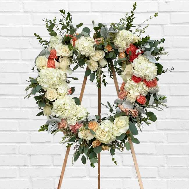 Heart-shaped floral wreath on a wooden stand with white and peach flowers