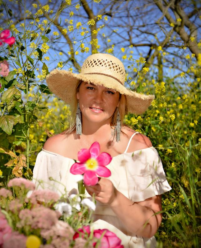 Woman in a straw hat holding a pink flower in a field of yellow blooms