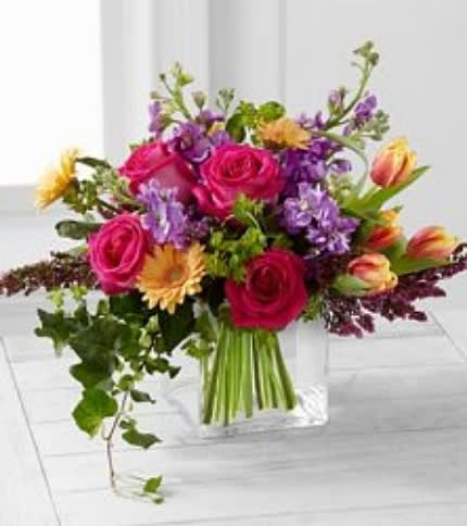 Bouquet of pink roses, purple flowers, and yellow blooms in a clear vase