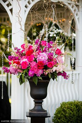 Tall pink and red floral arrangement in a dark urn on a pedestal
