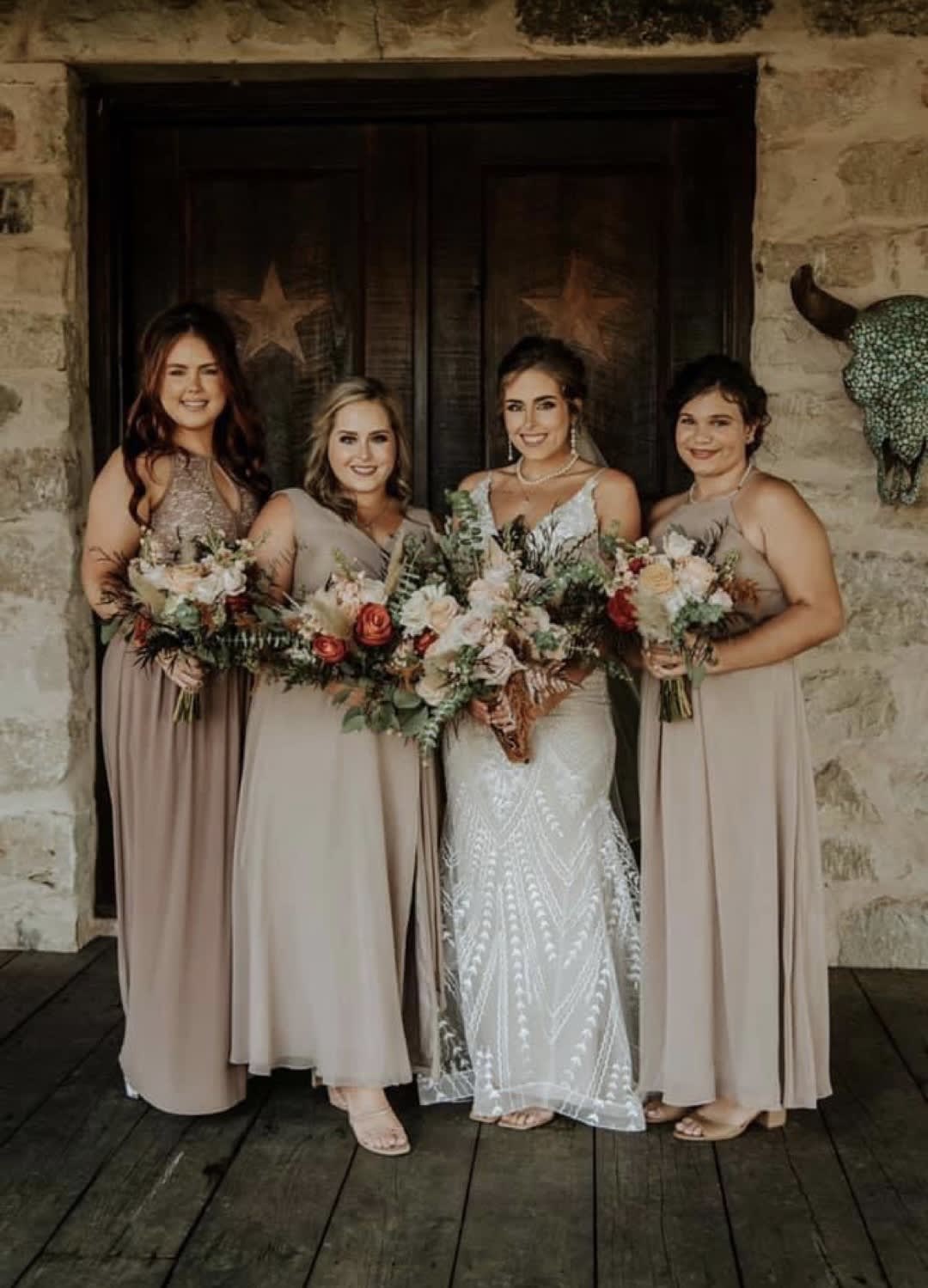 Bride and three bridesmaids holding mixed bouquets in front of a rustic doorway