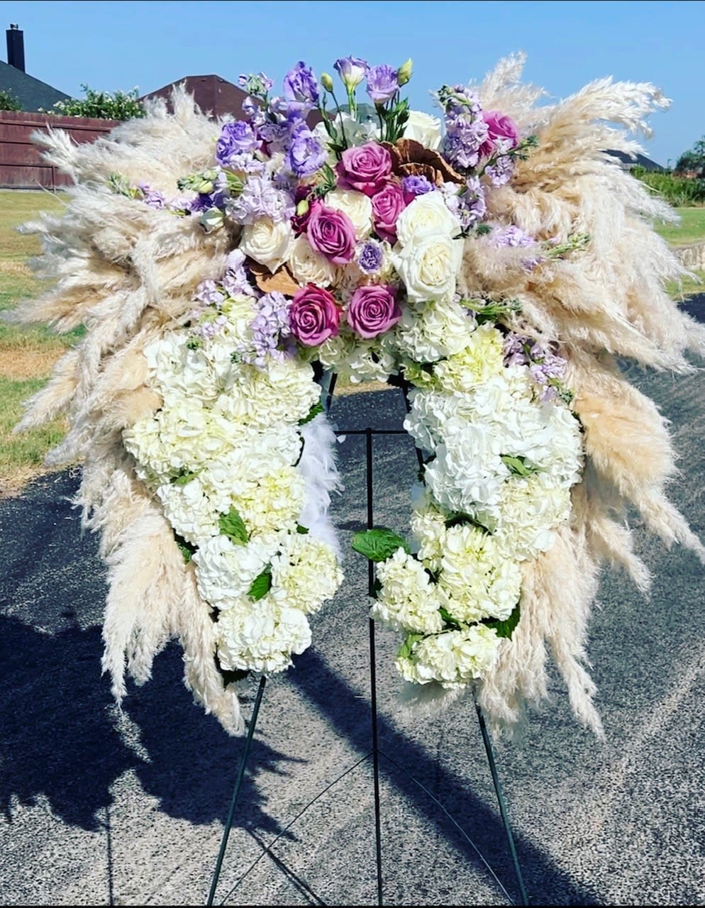 Large floral funeral spray with white hydrangeas, purple roses, and pampas grass