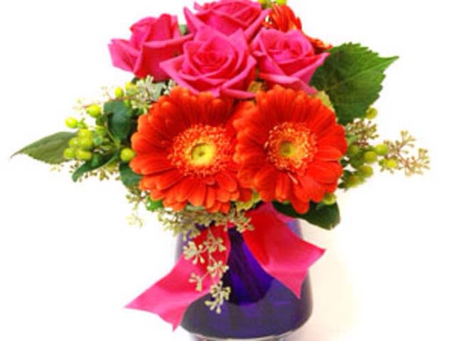 Bouquet of pink roses and orange gerbera daisies in a purple vase
