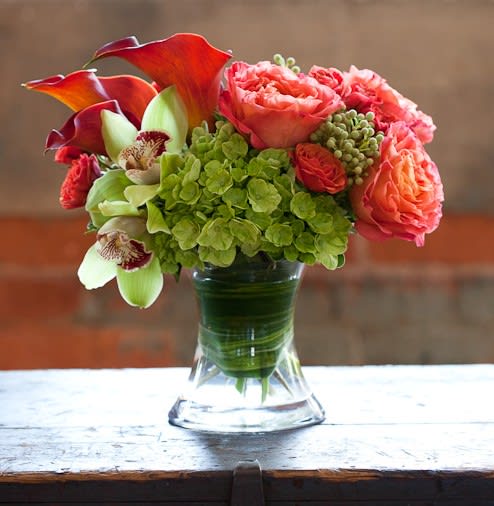 Bouquet of coral roses, green hydrangea, and calla lilies in a glass vase