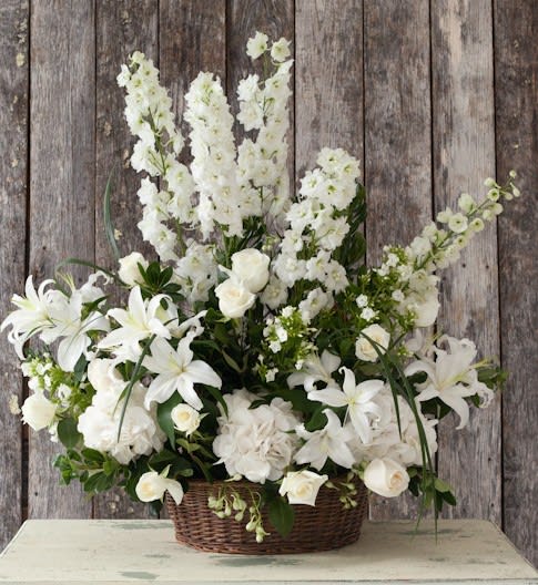 White floral arrangement in a wicker basket with lilies and roses