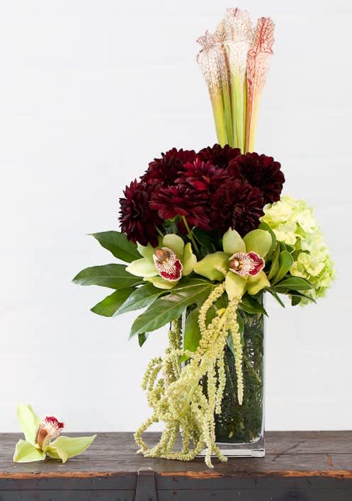 Tall floral arrangement with burgundy blooms, pale orchids, and a clear vase