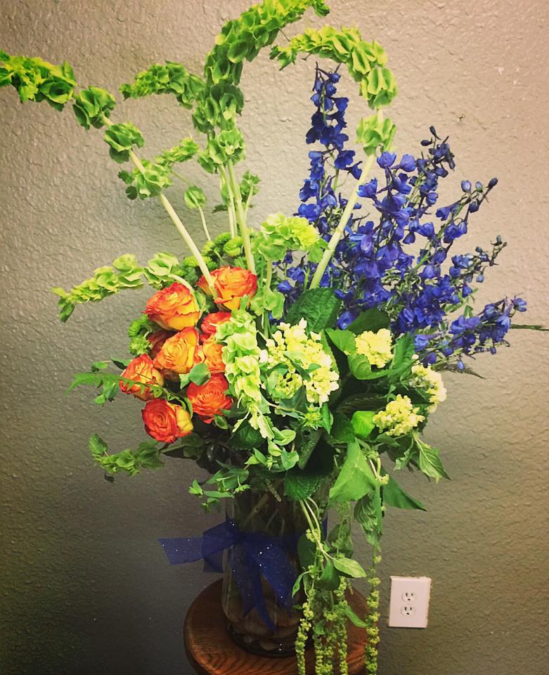 Tall bouquet of orange roses and blue delphinium in a glass vase