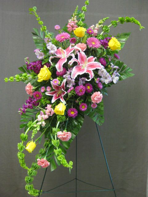 Standing floral spray with pink lilies, yellow roses, and purple blooms
