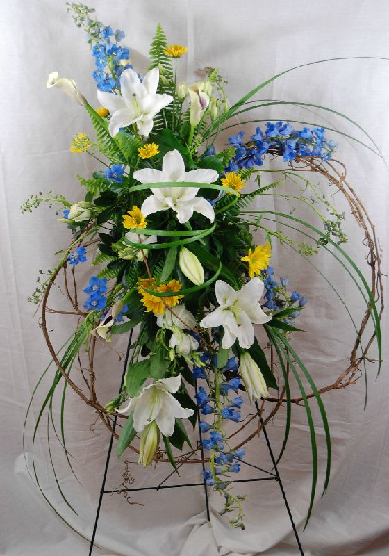 Tall floral arrangement with white lilies, blue flowers, and yellow accents on a stand