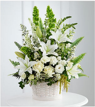Tall white lily and rose arrangement with green accents in a white woven basket