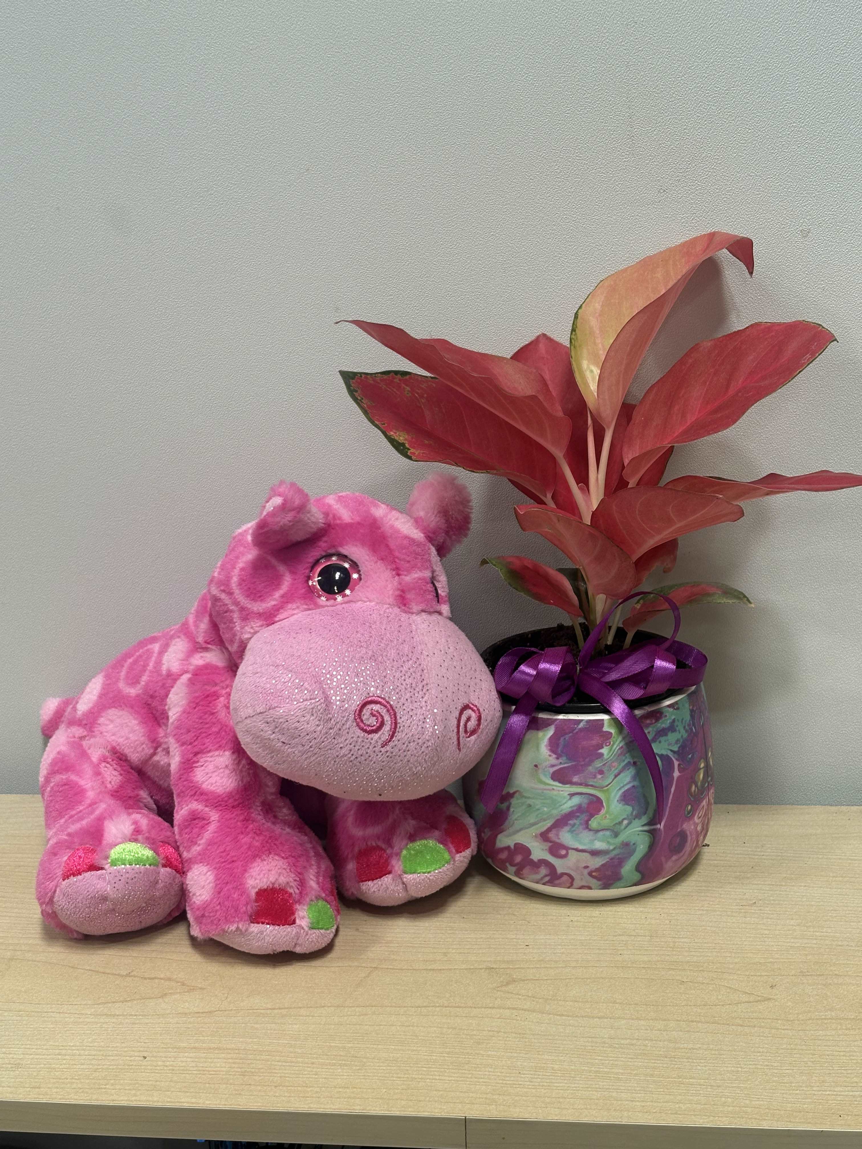 Pink plush hippo beside a potted red plant with a purple ribbon