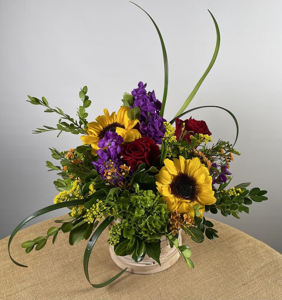 Bouquet of sunflowers, red roses, and purple flowers in a white basket