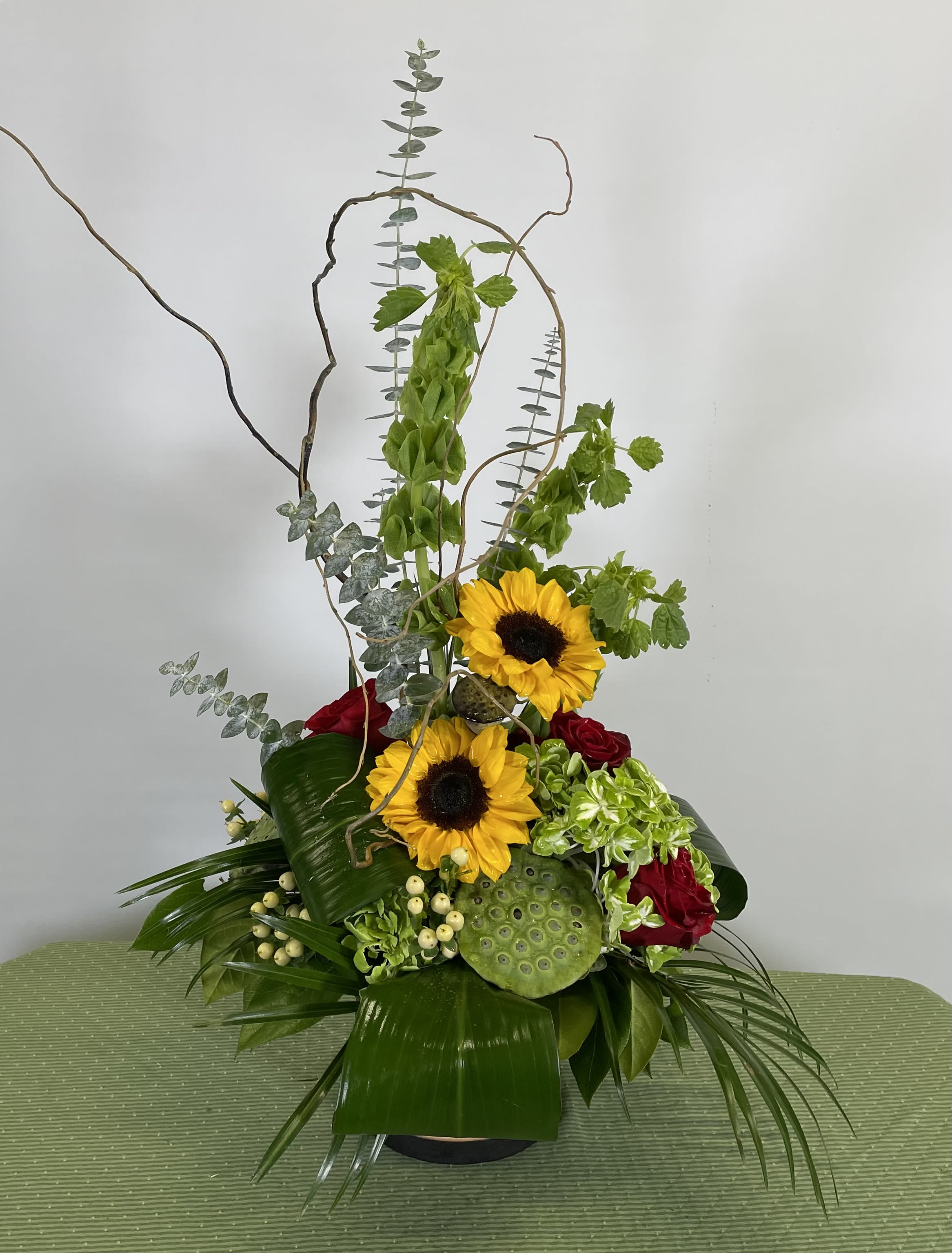Tall floral arrangement with sunflowers and red roses in a black vase