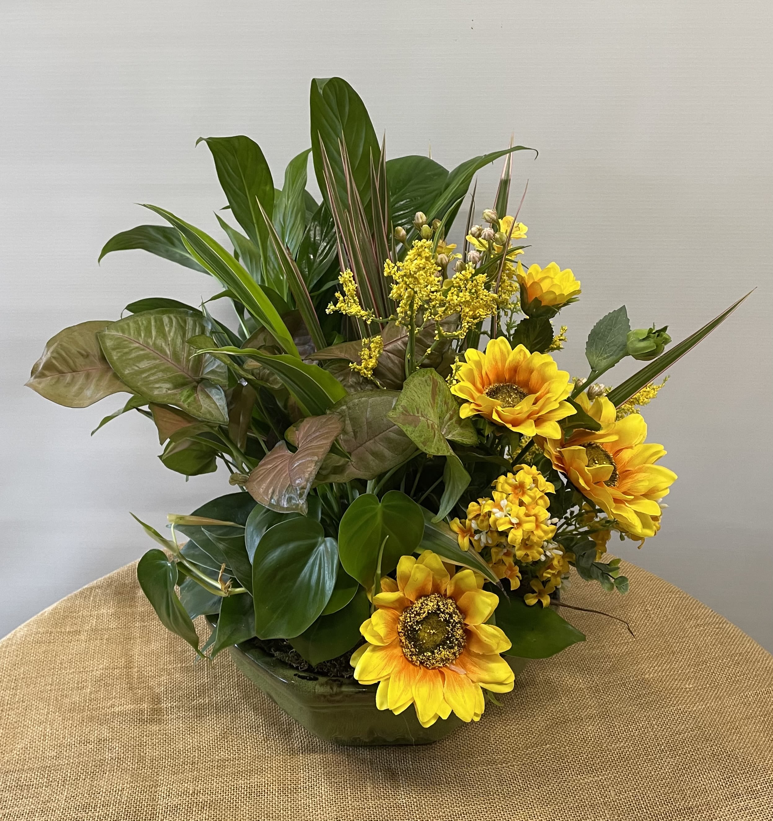 Yellow sunflowers arranged in a low glass bowl with mixed green foliage