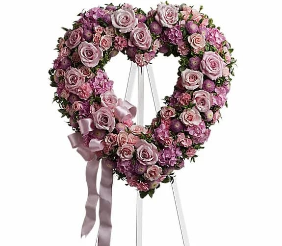 Heart-shaped floral wreath of pink and lavender roses on a stand with ribbon