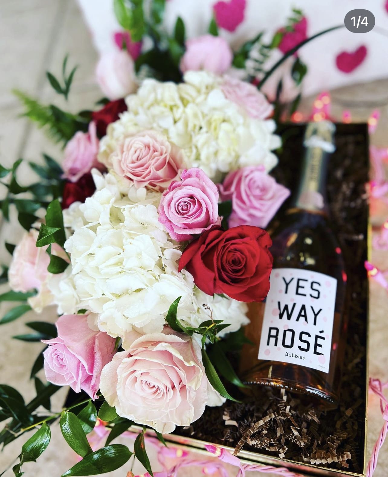 Pink and red roses with white hydrangeas beside a bottle of rosé