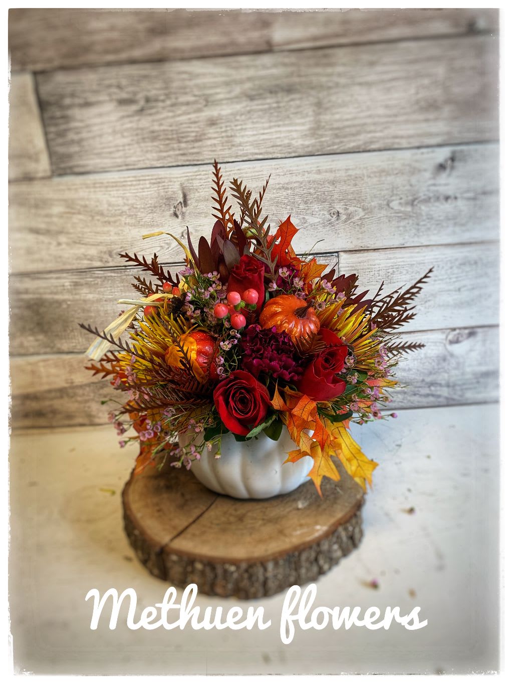Autumn floral arrangement in a white pumpkin container with red roses and fall leaves