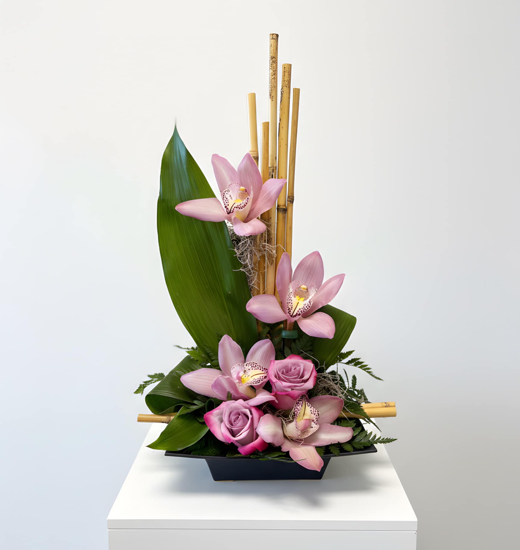 Pink orchids and roses arranged in a black container with bamboo accents