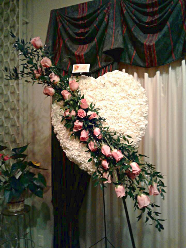 Heart-shaped white floral spray with pink roses on a stand