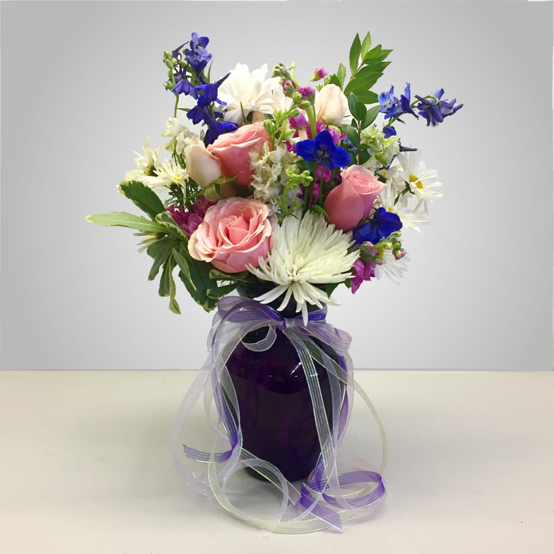 Bouquet of pink roses, white daisies, and blue flowers in a purple vase