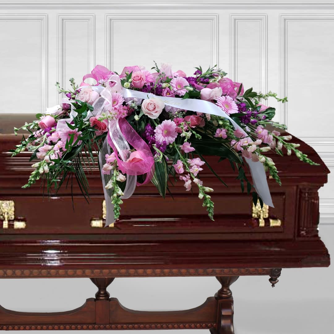 Pink floral spray on a casket with white ribbons